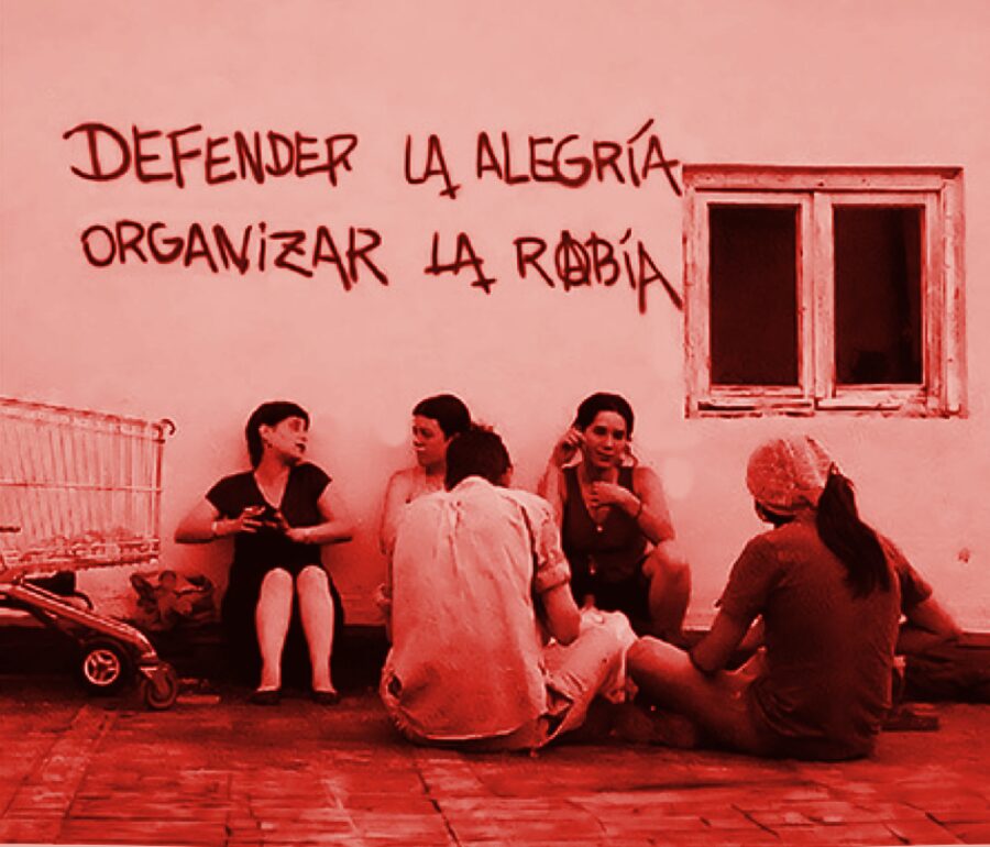 Mujeres sentadas ante una pared con la pintada «Defender la alegría, organizar la rabia»